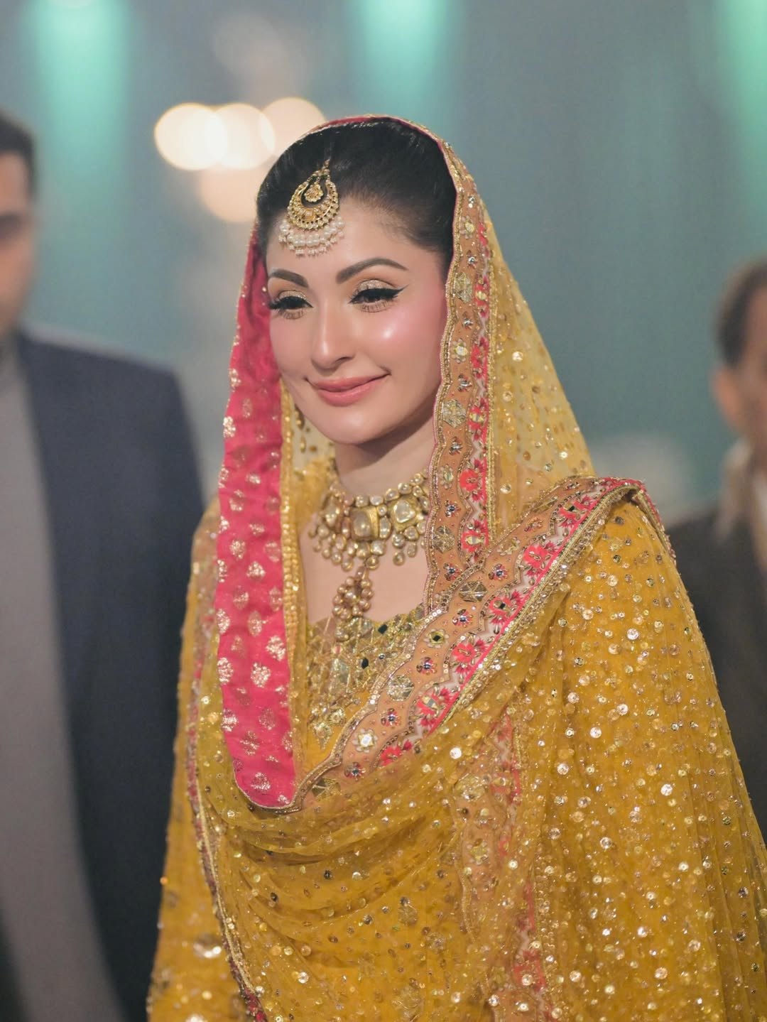Luxury mustard yellow bridal lehenga choli featuring intricate hand embellishments with detailed floral embroidery in soft pastel hues along the lehenga border, paired with a heavily adorned net dupatta with contrasting pink and gold border and a finely embellished choli, perfect for mehndi, mayun, dholki, and wedding festivities.