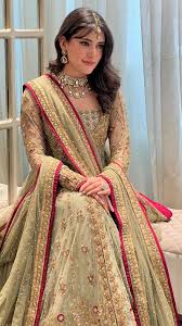 Haris Shakeel pistachio green lehenga choli featuring intricate gold embroidery, delicate hand embellishments, fine zari, sequins, and detailed floral motifs on a soft pastel base, paired with a full-sleeved embellished choli and a sheer net dupatta with rich gold detailing and a contrasting deep pink border, perfect for nikah, engagement, walima, and formal wedding events.