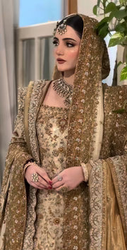 Haris Shakeel Mahrani ivory-gold bridal ensemble featuring a long heavily embellished shirt with intricate handwork including zardozi, dabka, naqshi, and delicate sequin detailing forming graceful floral and traditional motifs, paired with a magnificently worked dupatta with dense borders and finely finished edges, perfect for bridal wear with statement jewelry and traditional headpiece.