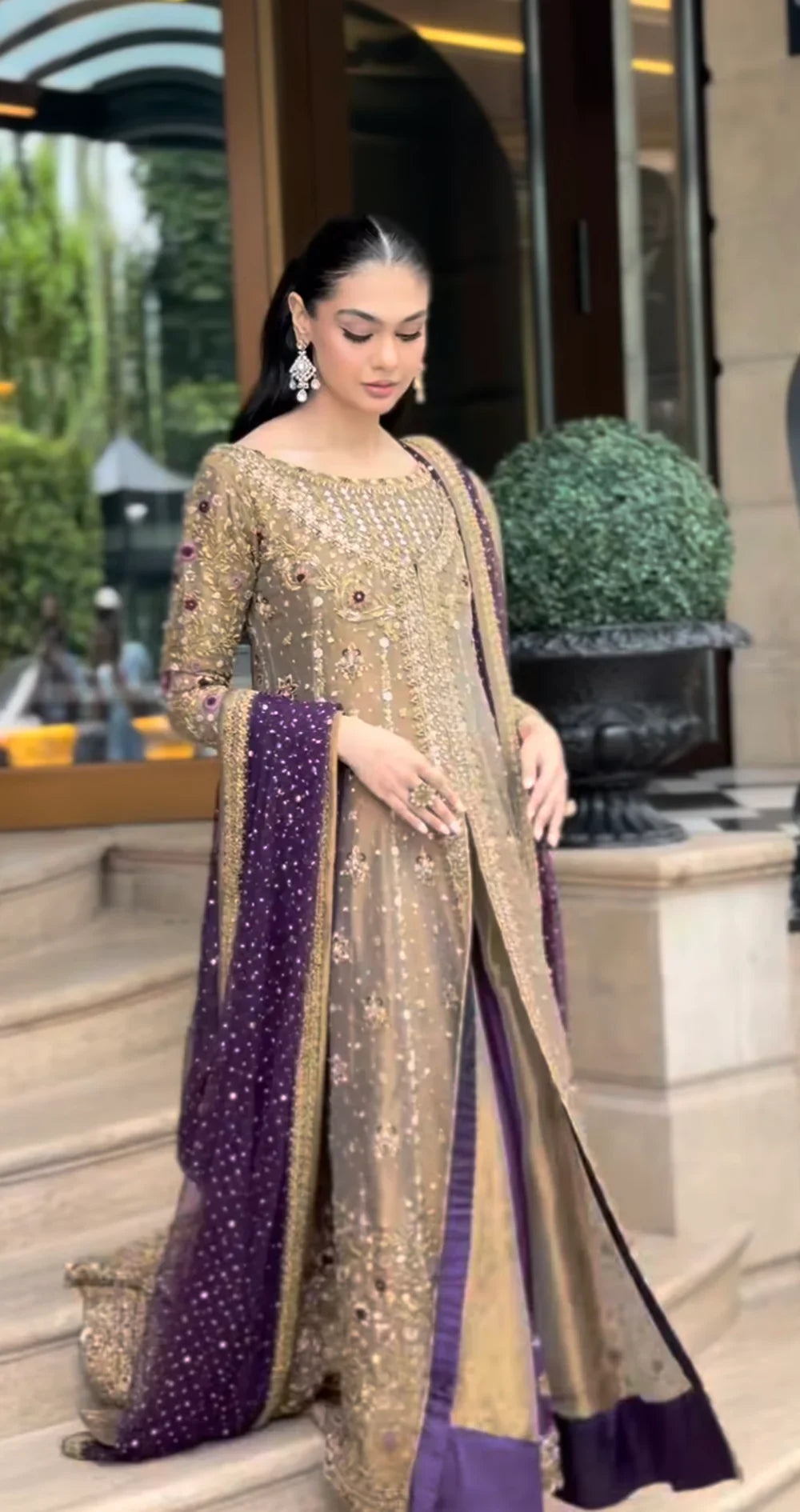 Haris Shakeel Aroha brushed bronze wedding ensemble featuring a luminous antique gold and soft champagne formal outfit with intricate hand embellishments and detailed embroidery, paired with a rich deep purple dupatta for a regal contrast, perfect for weddings, receptions, engagements, and formal celebrations.