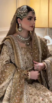 Haris Shakeel Mahrani ivory-gold bridal ensemble featuring a long heavily embellished shirt with intricate handwork including zardozi, dabka, naqshi, and delicate sequin detailing forming graceful floral and traditional motifs, paired with a magnificently worked dupatta with dense borders and finely finished edges, perfect for bridal wear with statement jewelry and traditional headpiece.