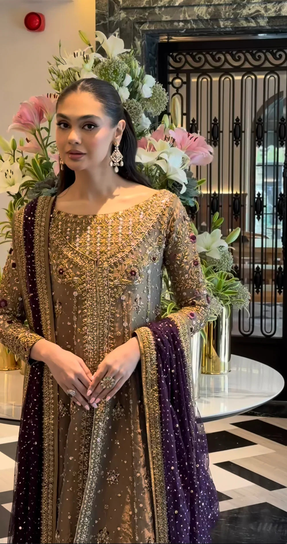 Haris Shakeel Aroha brushed bronze wedding ensemble featuring a luminous antique gold and soft champagne formal outfit with intricate hand embellishments and detailed embroidery, paired with a rich deep purple dupatta for a regal contrast, perfect for weddings, receptions, engagements, and formal celebrations.