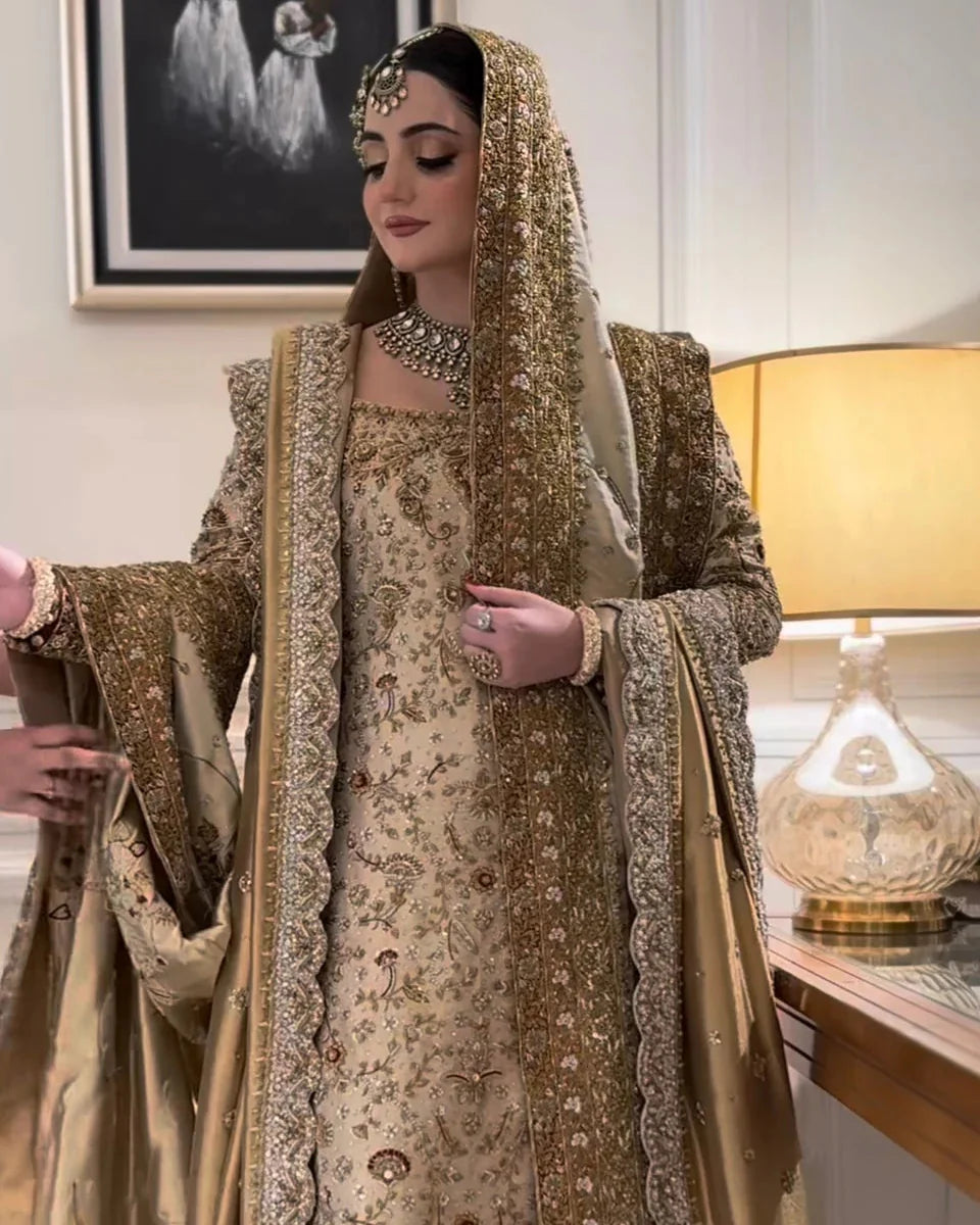 Haris Shakeel Mahrani ivory-gold bridal ensemble featuring a long heavily embellished shirt with intricate handwork including zardozi, dabka, naqshi, and delicate sequin detailing forming graceful floral and traditional motifs, paired with a magnificently worked dupatta with dense borders and finely finished edges, perfect for bridal wear with statement jewelry and traditional headpiece.