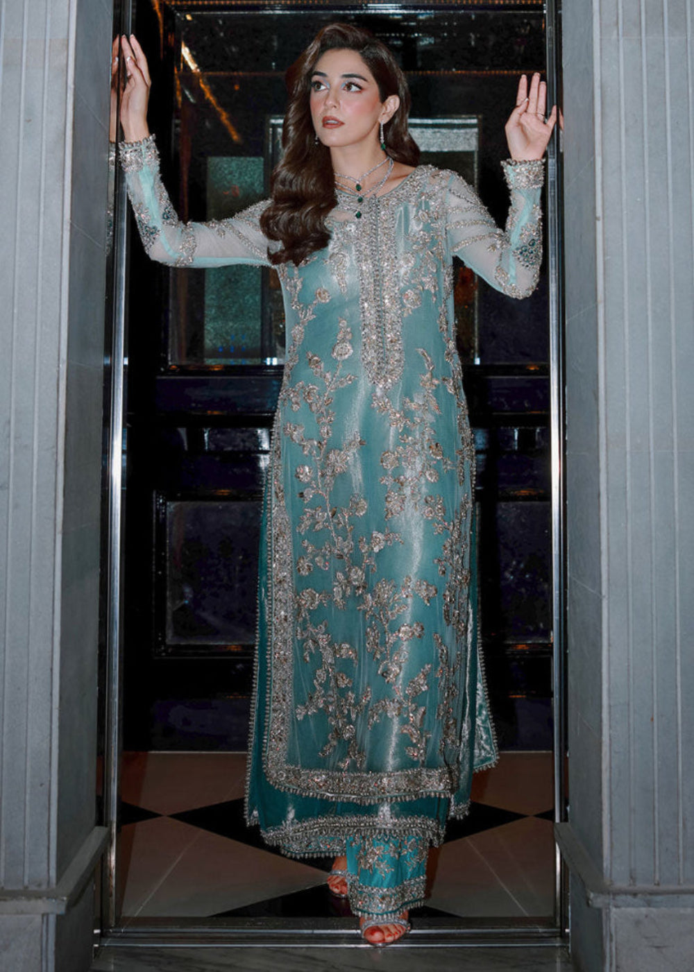 Sara Rohale Asghar Ferozeah aqua long shirt featuring intricate silver embellishments with hand-embroidered floral motifs creating a refined jal, paired with a sheer dupatta with heavily embellished border and scattered sequins, and straight-cut azar trousers with bejeweled peacock hem in silver threadwork, perfect for formal occasions and statement looks.