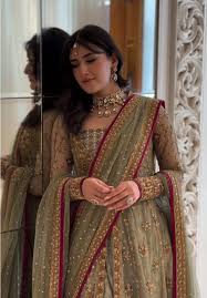  Haris Shakeel pistachio green lehenga choli featuring intricate gold embroidery, delicate hand embellishments, fine zari, sequins, and detailed floral motifs on a soft pastel base, paired with a full-sleeved embellished choli and a sheer net dupatta with rich gold detailing and a contrasting deep pink border, perfect for nikah, engagement, walima, and formal wedding events.