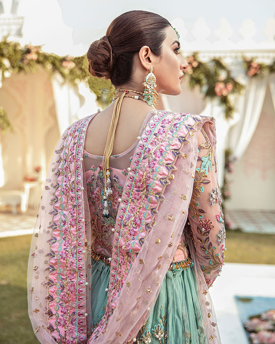 Joli Rajkumari lehenga choli in a unique color block of pink and sea green featuring intricately hand-worked embellishments with pearls, gotta, dabka, nakshi, crystals, mukaish, and pitta, paired with a pink tulle dupatta filled with booti spray and four-sided silk borders with heavy pearl tassel details, inspired by Rajasthani culture.